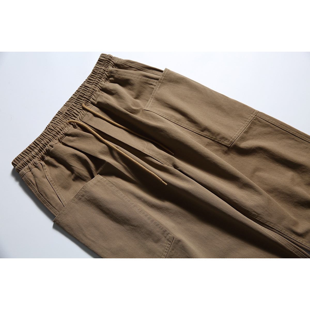 Close-up of brown cargo pants showing the elastic waistband, drawcord, stitching, and large patch pockets.