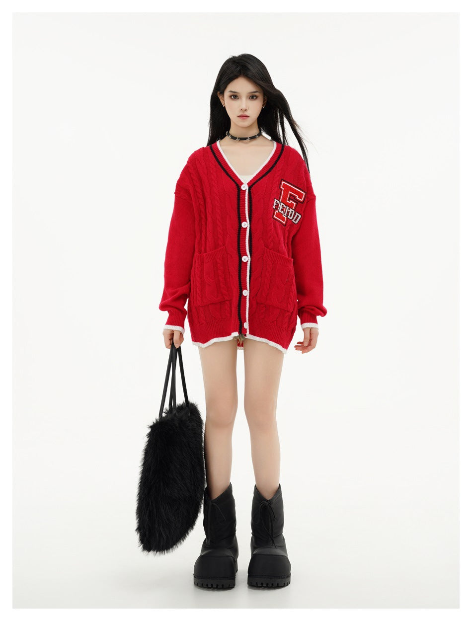 Front view of a model wearing a red cable-knit cardigan with white and black trim, buttons, pockets, and a chest patch.