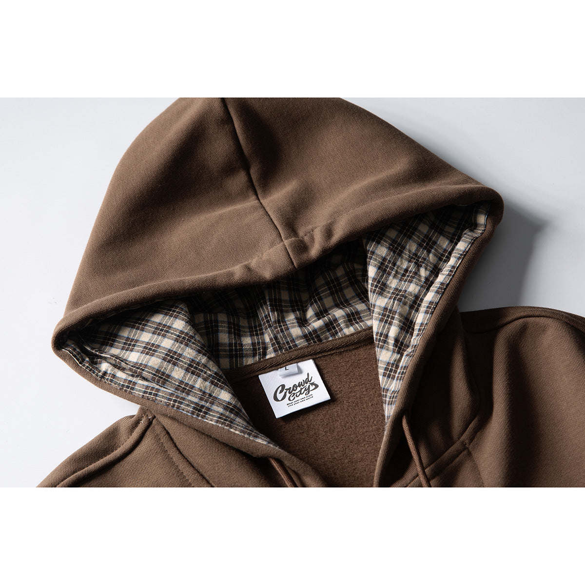 Close-up of a brown hoodie with beige-and-blue plaid hood lining and a sewn neck label.