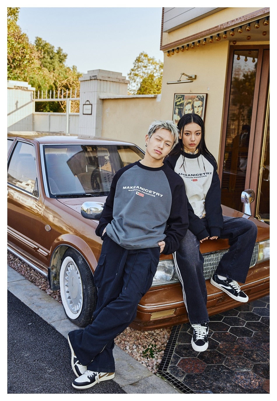 Two models wear gray and cream raglan sweatshirts with black sleeves beside a vintage car.