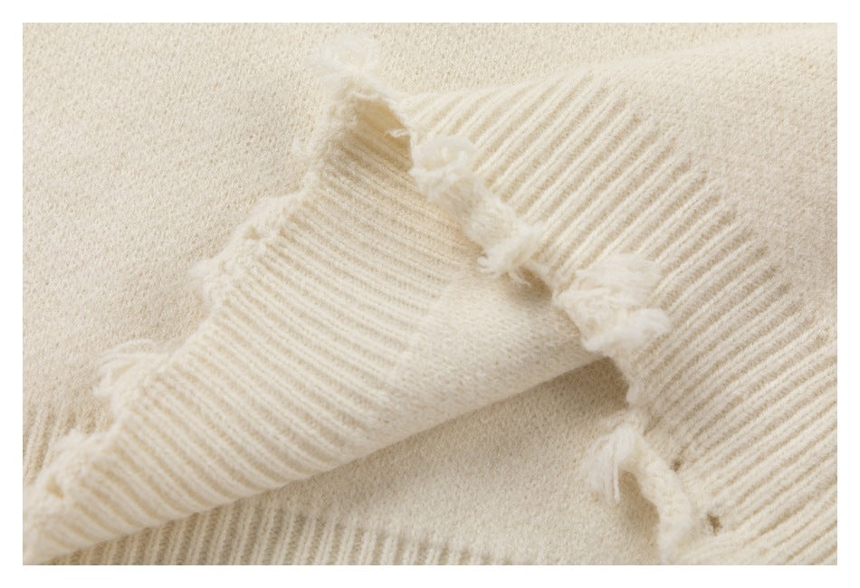 Close-up of a ribbed ivory sweater edge with distressed, frayed knit details.