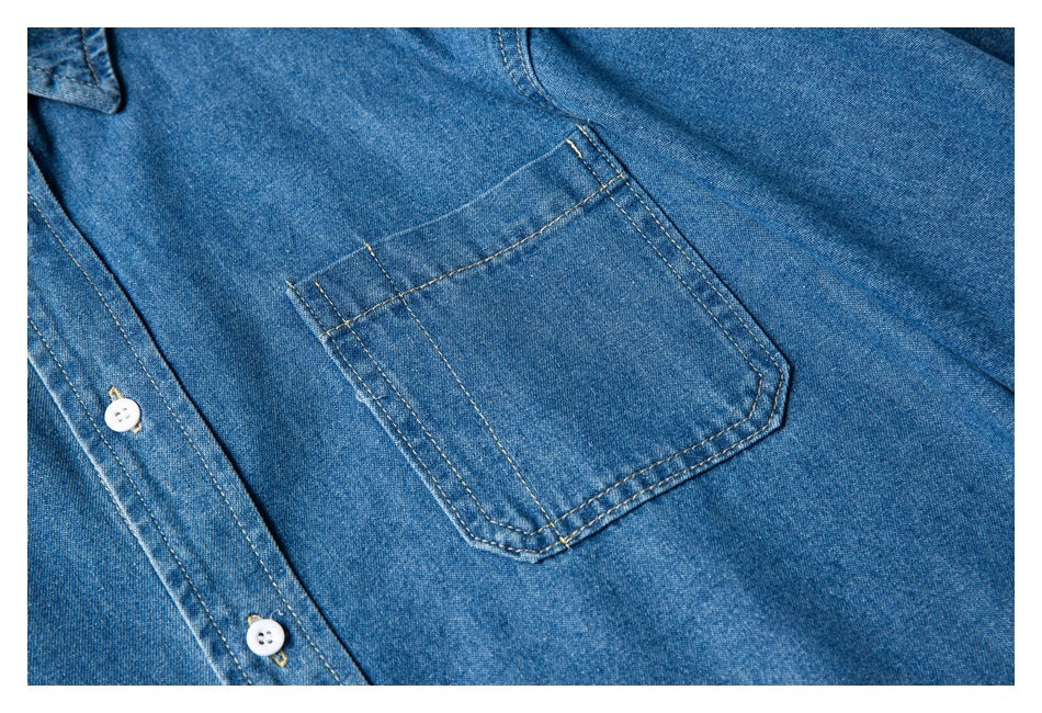 Close-up of a blue denim shirt's chest pocket, tan stitching, and white buttons.