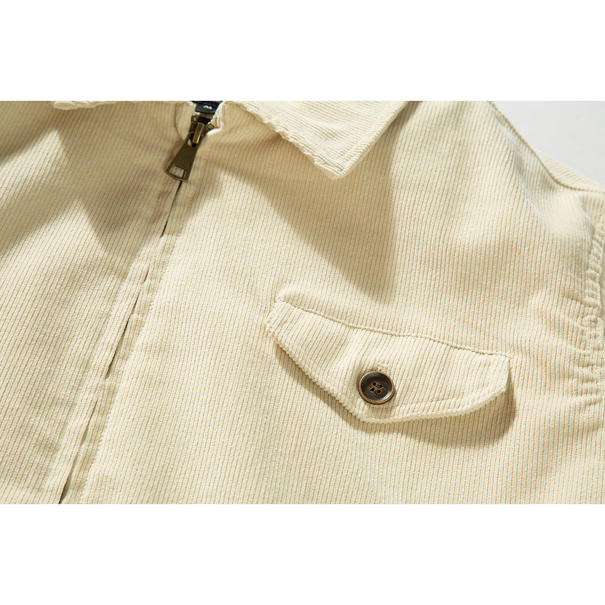 Close-up of a cream ribbed jacket showing its flap chest pocket and dark button.