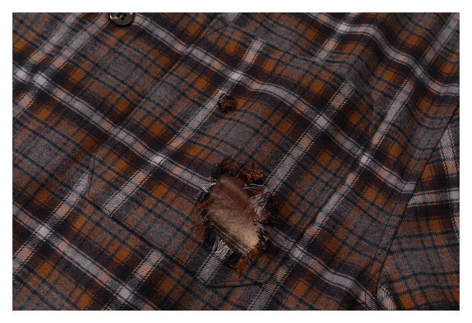 Close-up of gray, rust, and black plaid fabric showing a frayed distressed hole and nearby button.