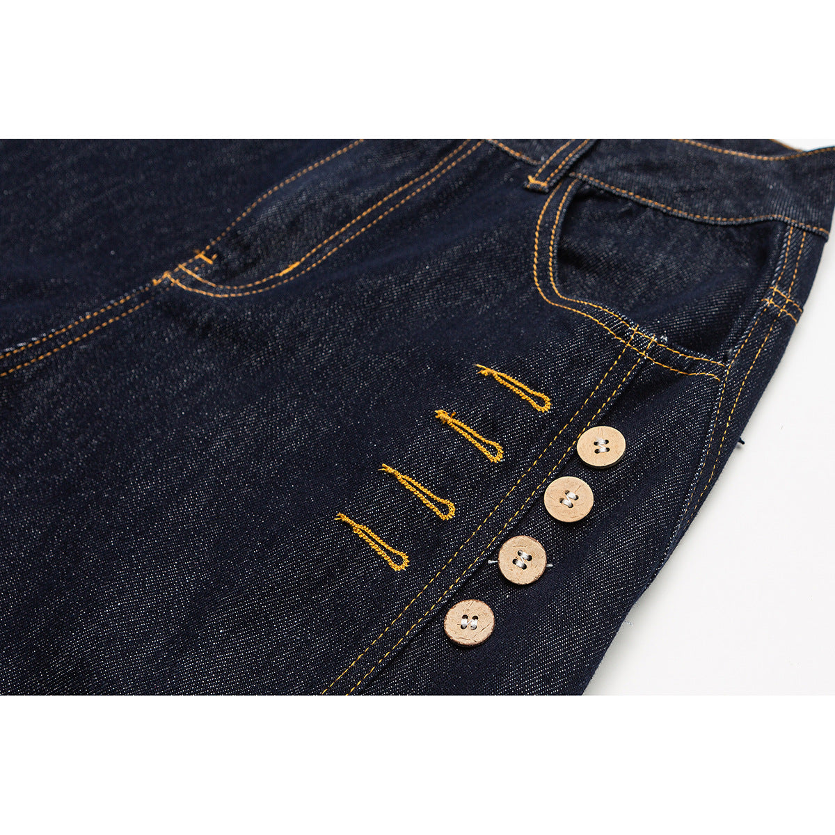 Close-up of dark indigo jeans showing a four-button fly and golden contrast stitching.