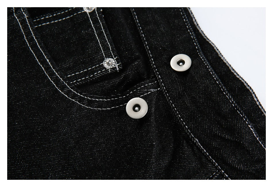 Close-up of black jeans showing two metal buttons, a small pocket, and white contrast stitching.