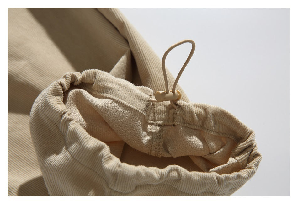 Close-up of a beige trouser hem drawcord with a cord lock and gathered ribbed fabric.