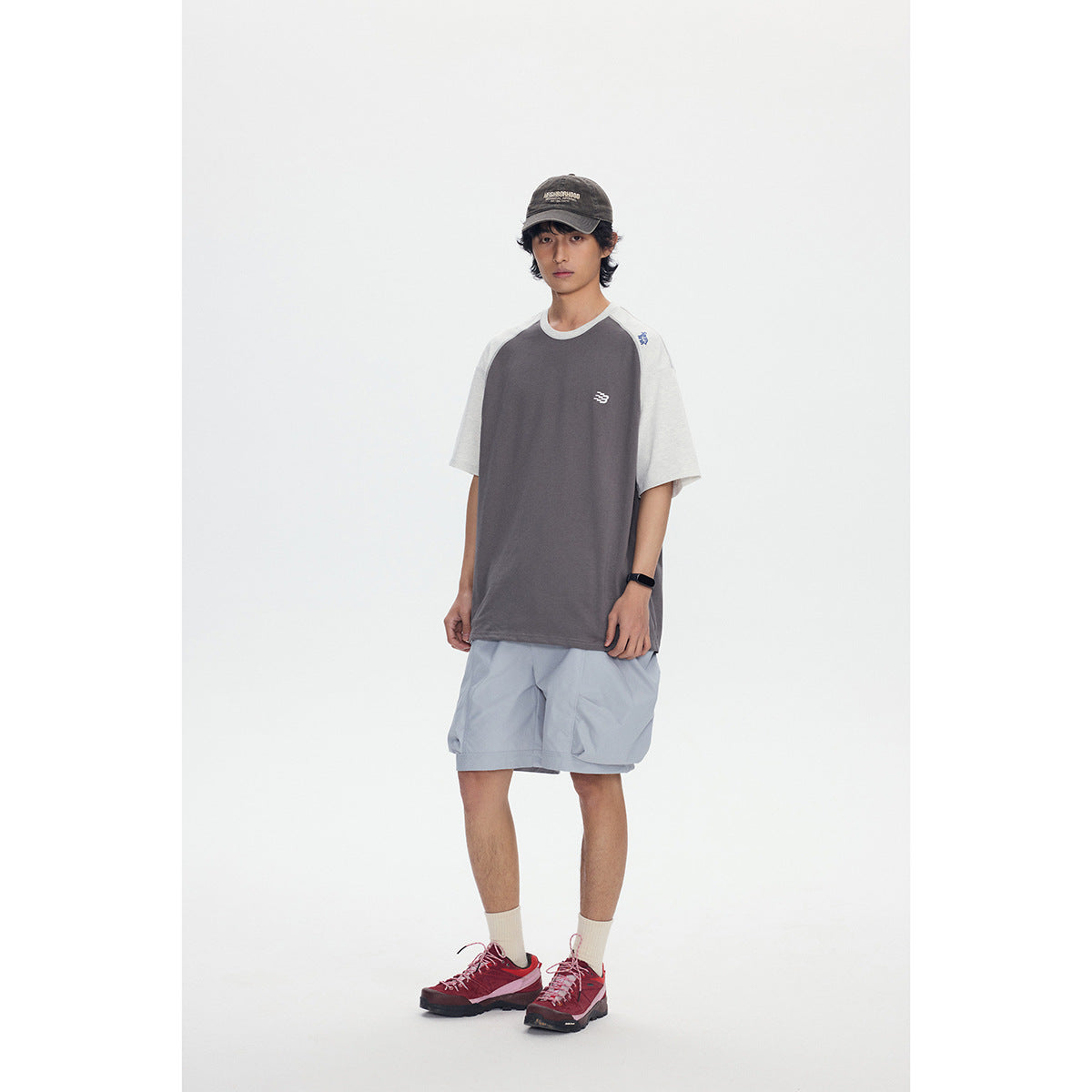 Full-length front view of a model wearing a charcoal T-shirt with light gray raglan sleeves and pale blue shorts.
