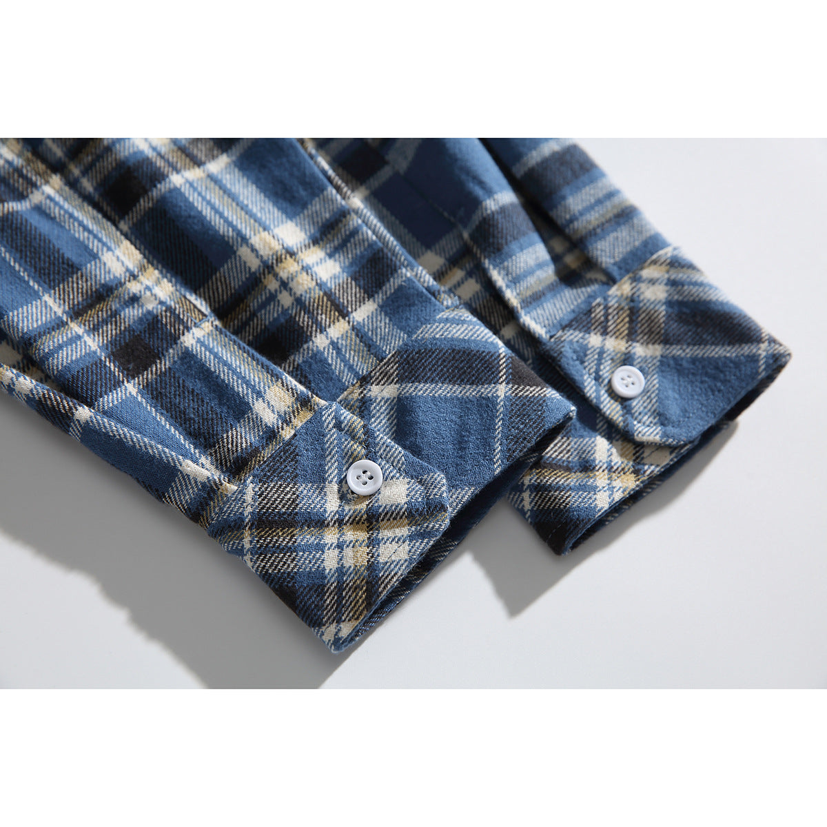Close-up of the buttoned cuffs on a blue, navy, and cream plaid shirt.