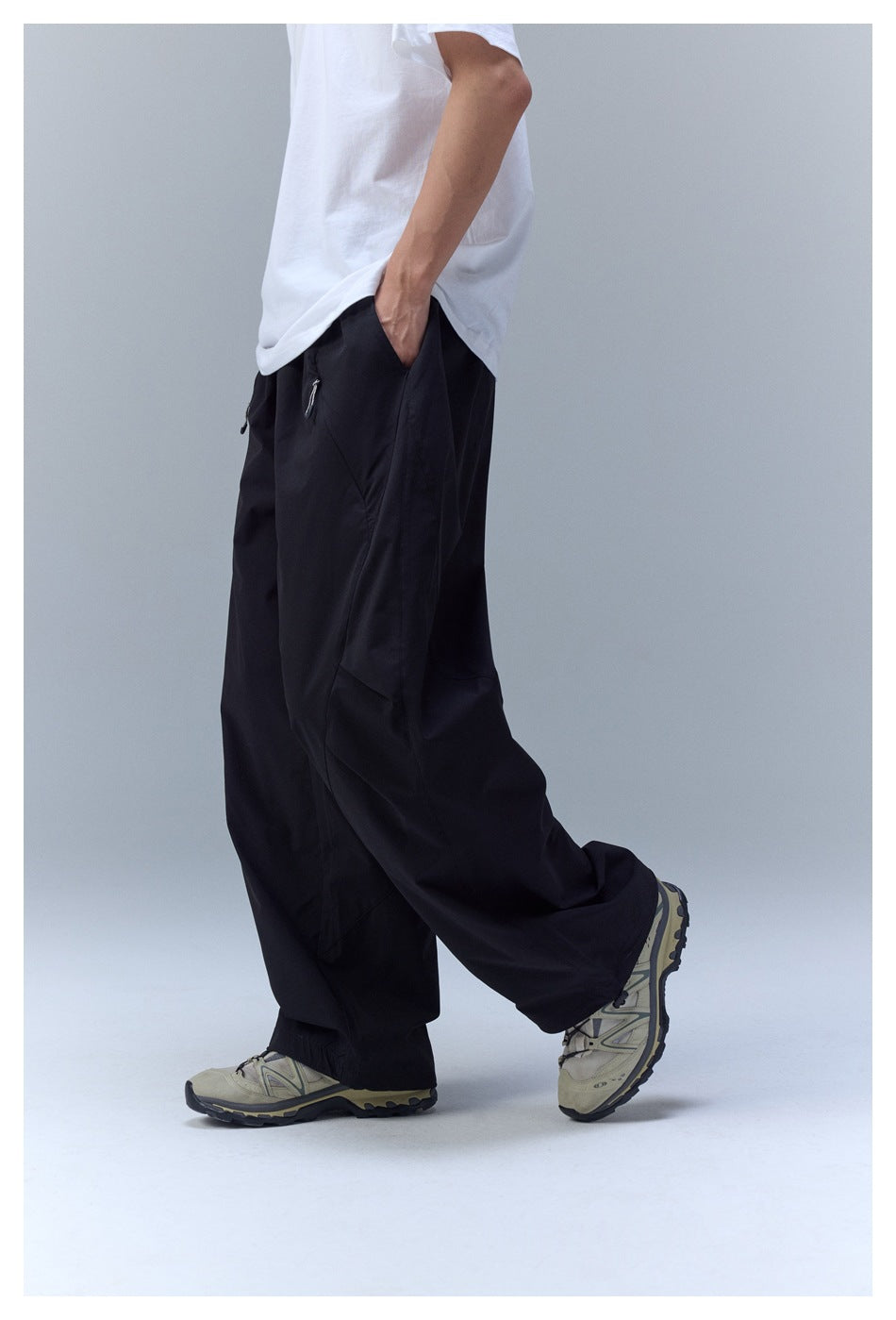 Side view of a model wearing loose black wide-leg pants with zip pockets and sneakers.