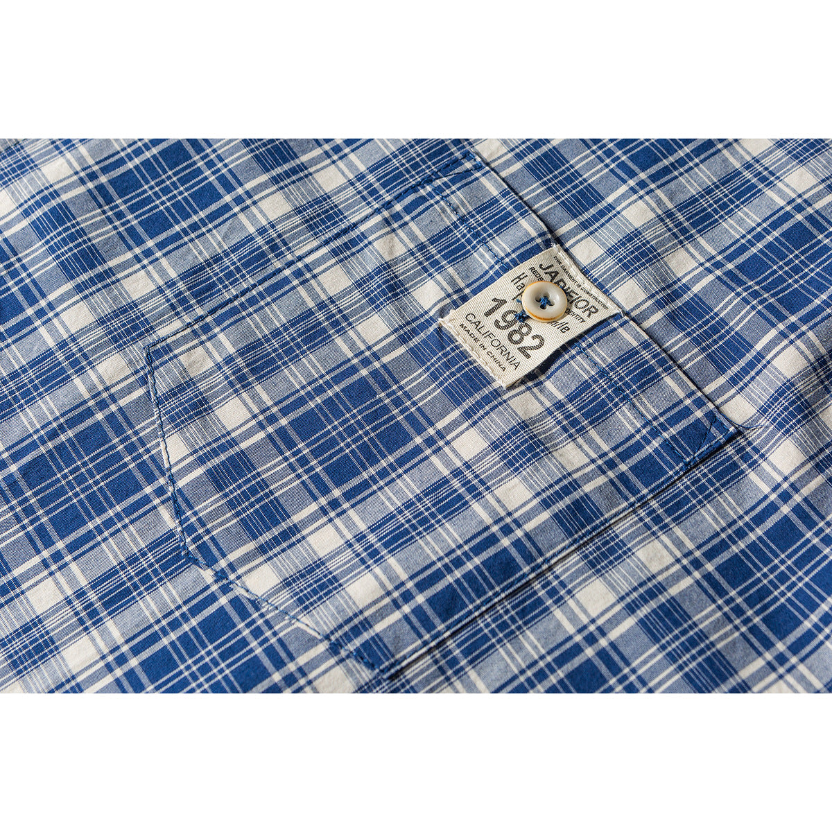 Close-up of a blue and white plaid shirt pocket with a sewn label and button.