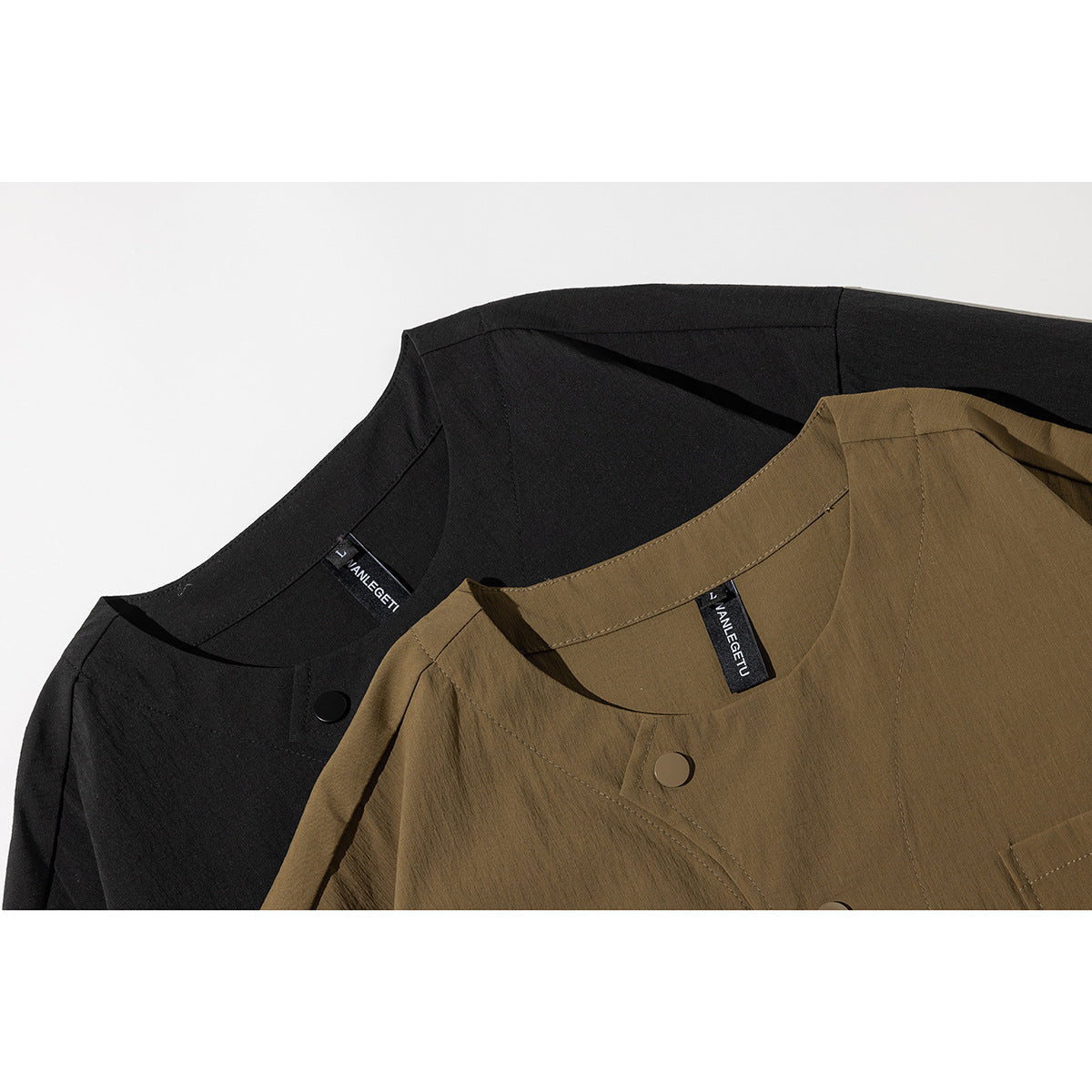 Close-up of black and olive-brown short-sleeve shirts showing their round necklines and front buttons.