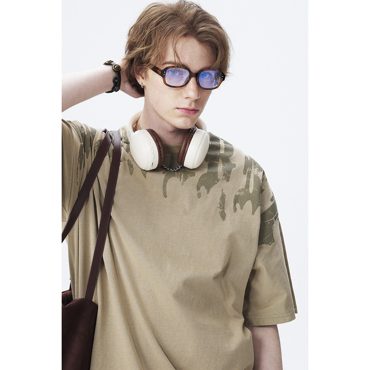 Close view of a model wearing a khaki oversized T-shirt with dark abstract shoulder print.