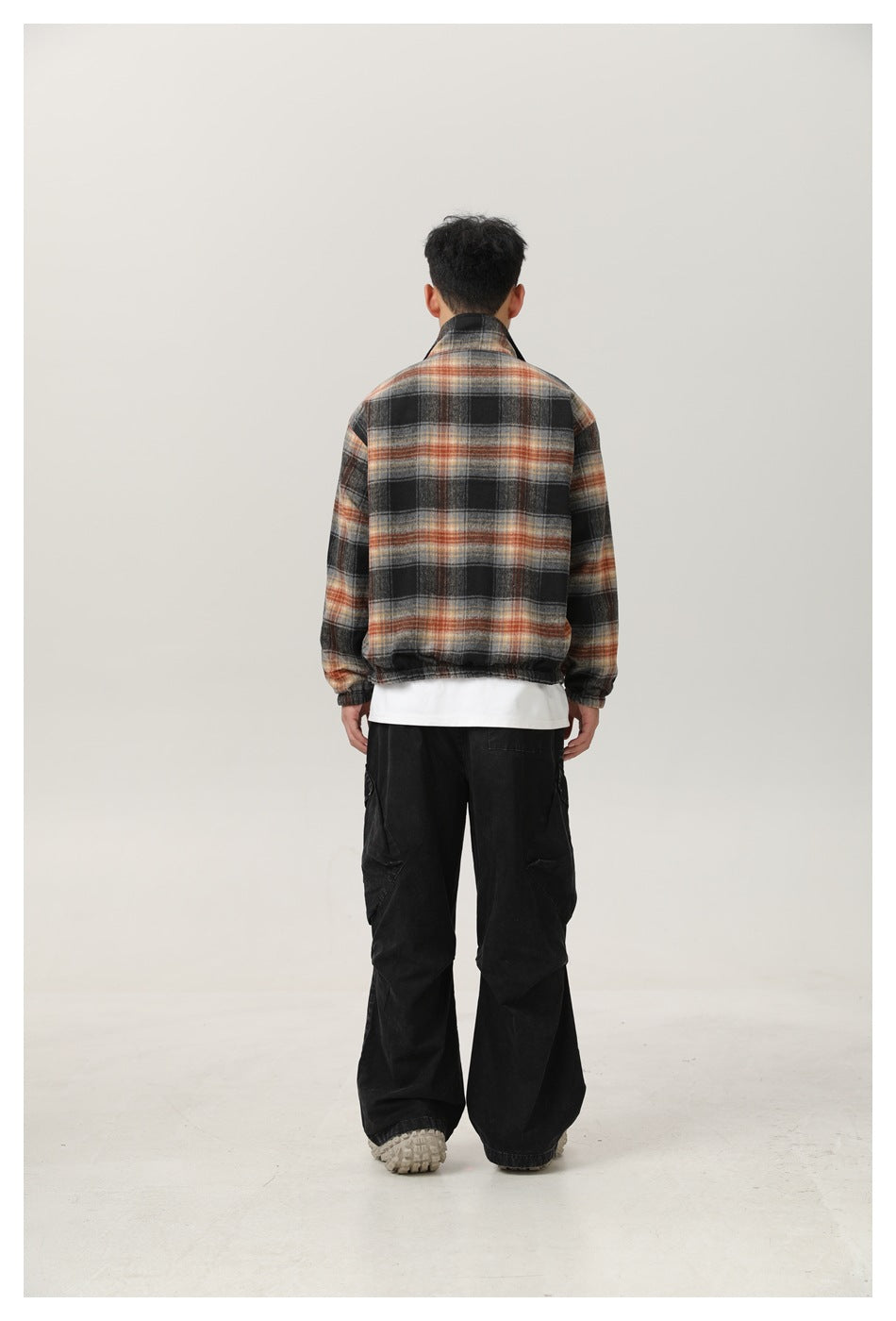 Rear view of a man wearing a black, gray, and rust plaid jacket with an elastic hem and cuffs.