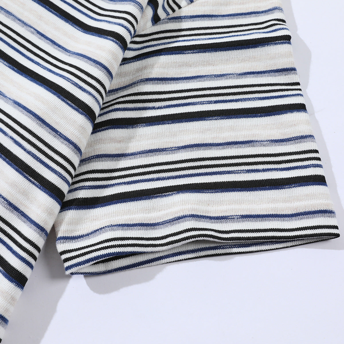 Close-up of a white knit T-shirt hem and sleeve with narrow black, navy, and gray horizontal stripes.