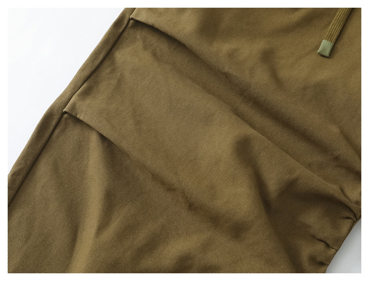 Close-up of olive-brown trousers showing textured fabric folds and the end of a drawcord.