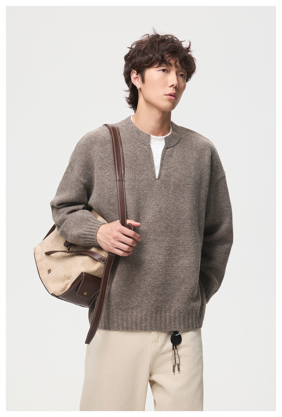 Model wearing a taupe oversized split-neck sweater with ribbed trim and a shoulder bag.