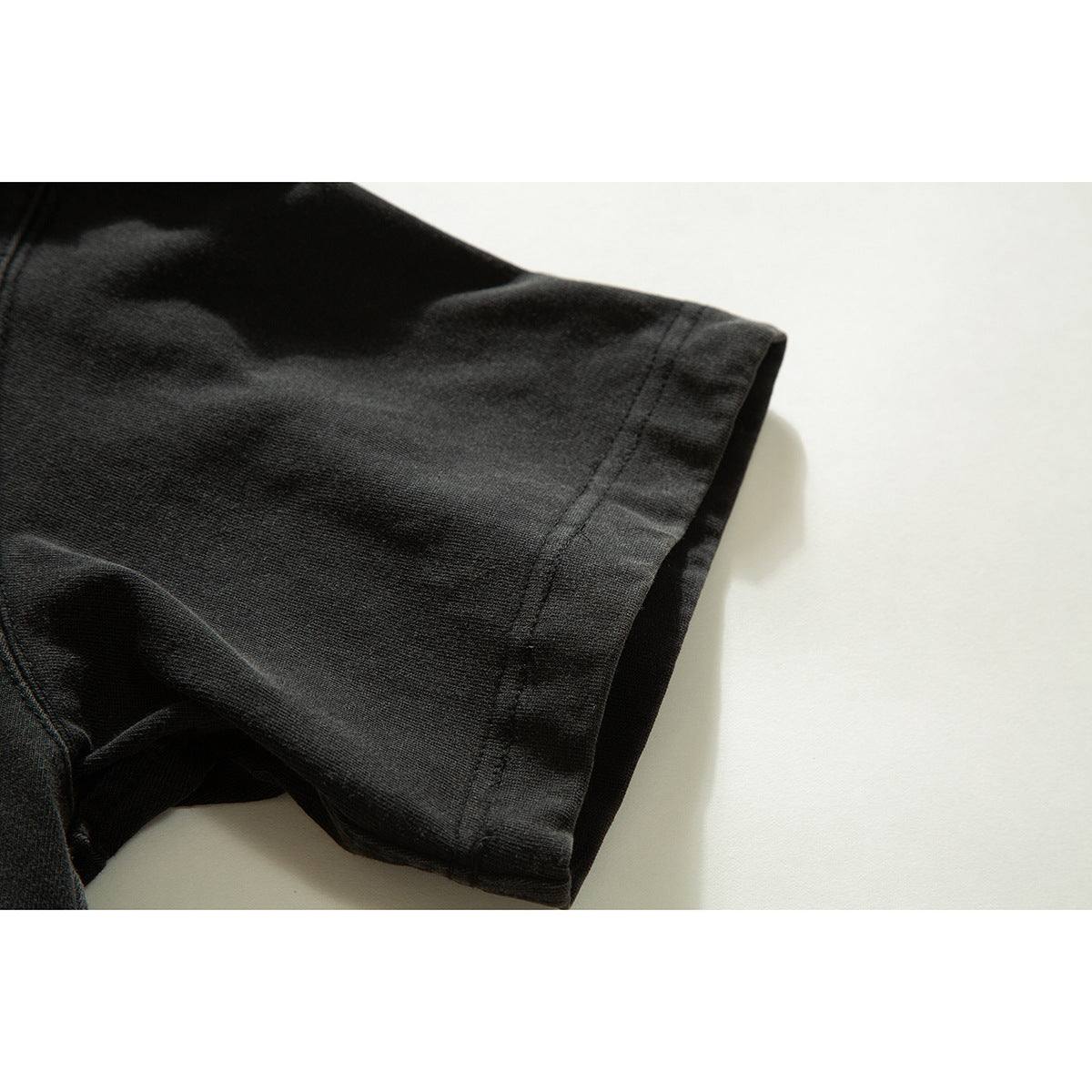 Close-up of the short sleeve and stitched hem of a dark charcoal shirt.