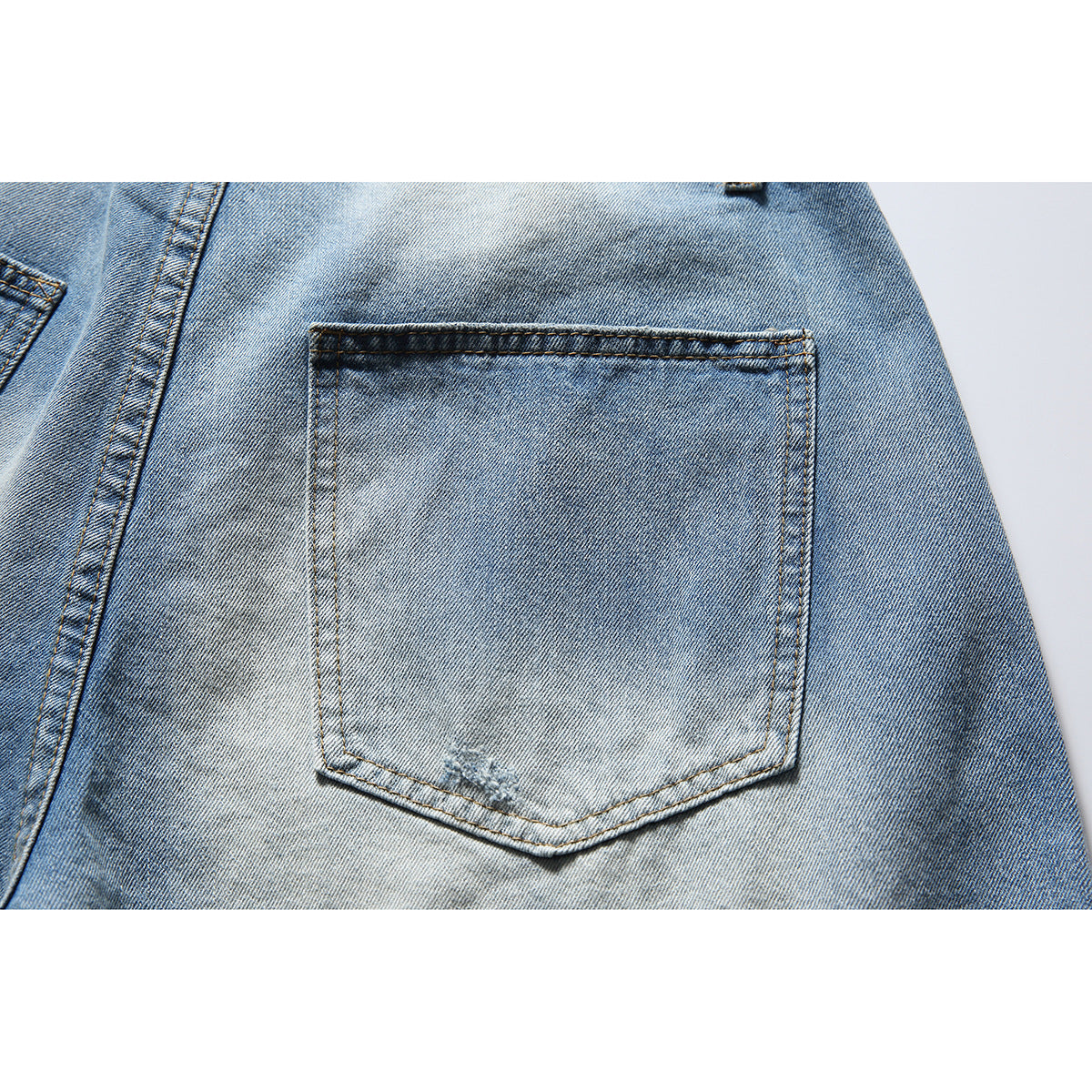 Close-up of a stitched back pocket on faded blue denim shorts.