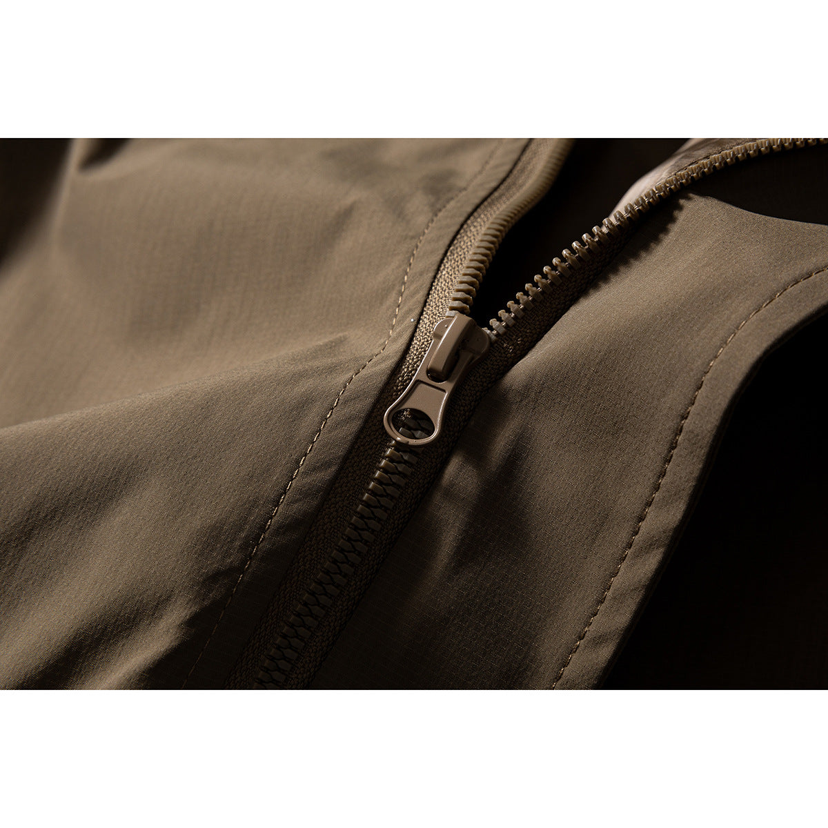 Close-up of a brown jacket's front zipper and surrounding stitched panels.