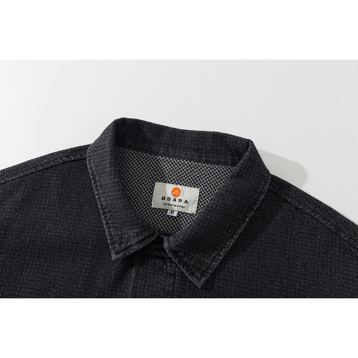 Close-up of the charcoal jacket's pointed collar, patterned inner facing, and sewn neck label.