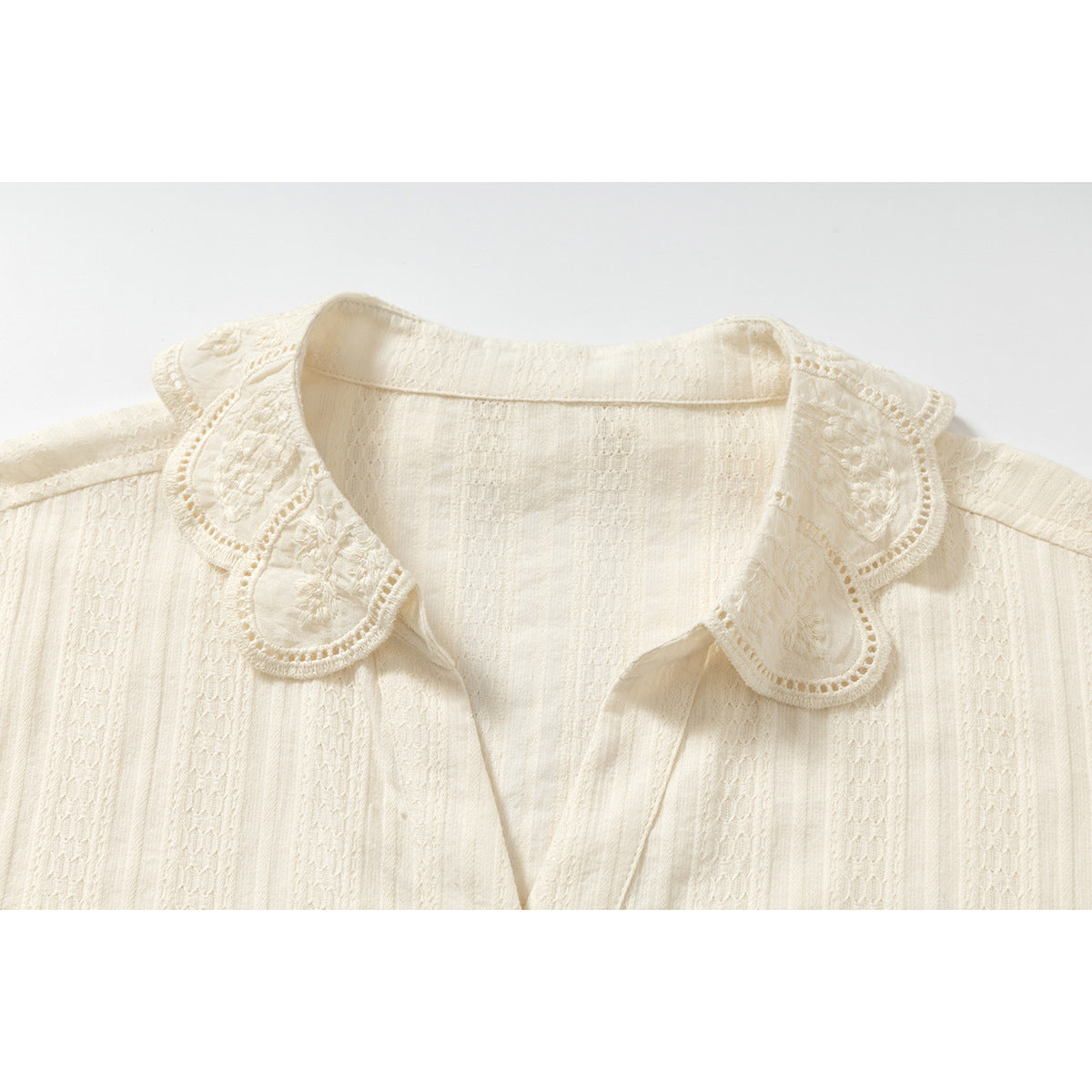 Close-up of an ivory shirt’s embroidered scalloped collar and textured vertical fabric pattern.