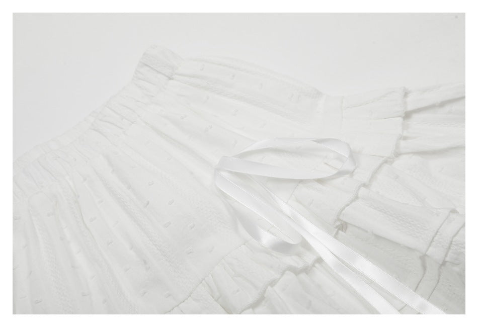 Close-up of a white tiered skirt's textured gathered waistband and long satin ties.