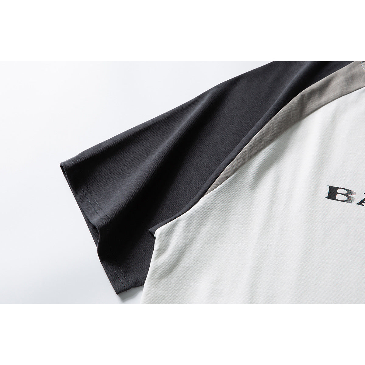 Close-up of a white color-block T-shirt with a charcoal sleeve and partial black chest lettering.