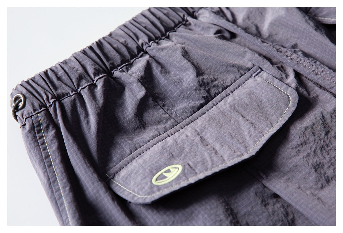 Close-up of a charcoal-gray pants flap pocket with pale stitching and a small lime emblem.