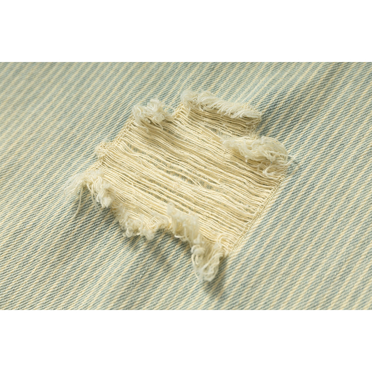 Close-up of a frayed distressed patch on pale blue striped fabric.