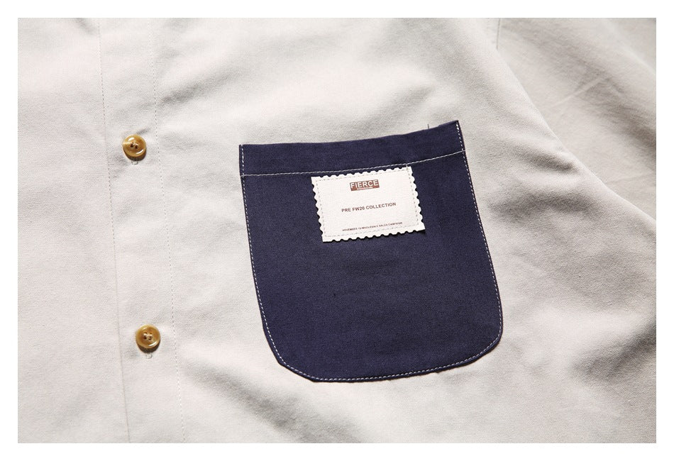Close-up of a navy chest pocket and tan buttons on a light beige shirt; a small label is attached to the pocket.