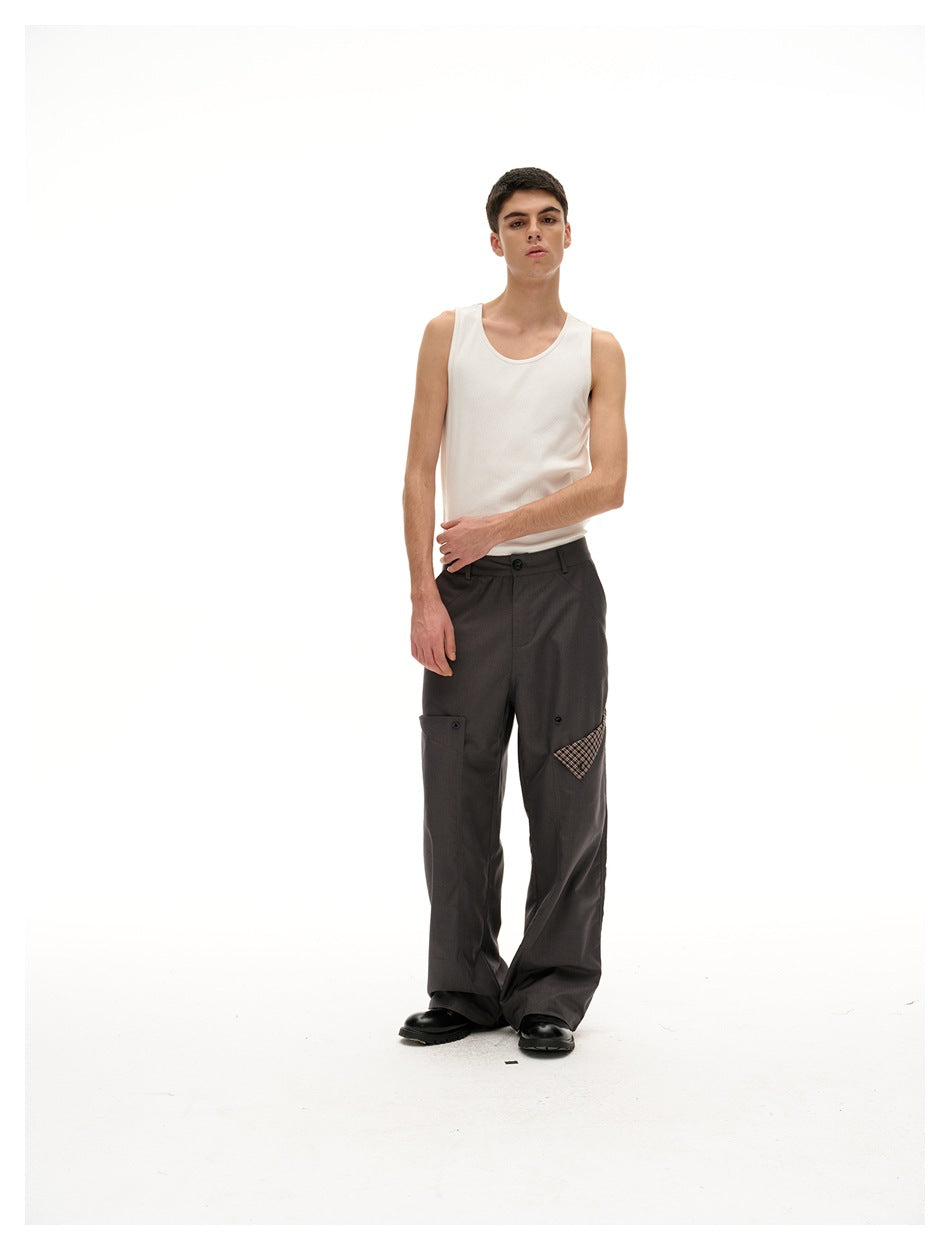 Model wearing a white tank top and charcoal wide-leg trousers with buttoned utility pockets and plaid accents.