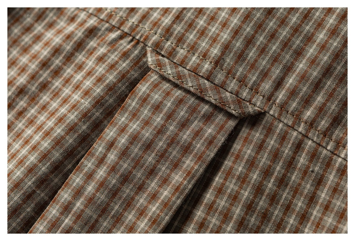 Close-up of a folded seam and overlapping fabric on a rust, gray, and white checked shirt.