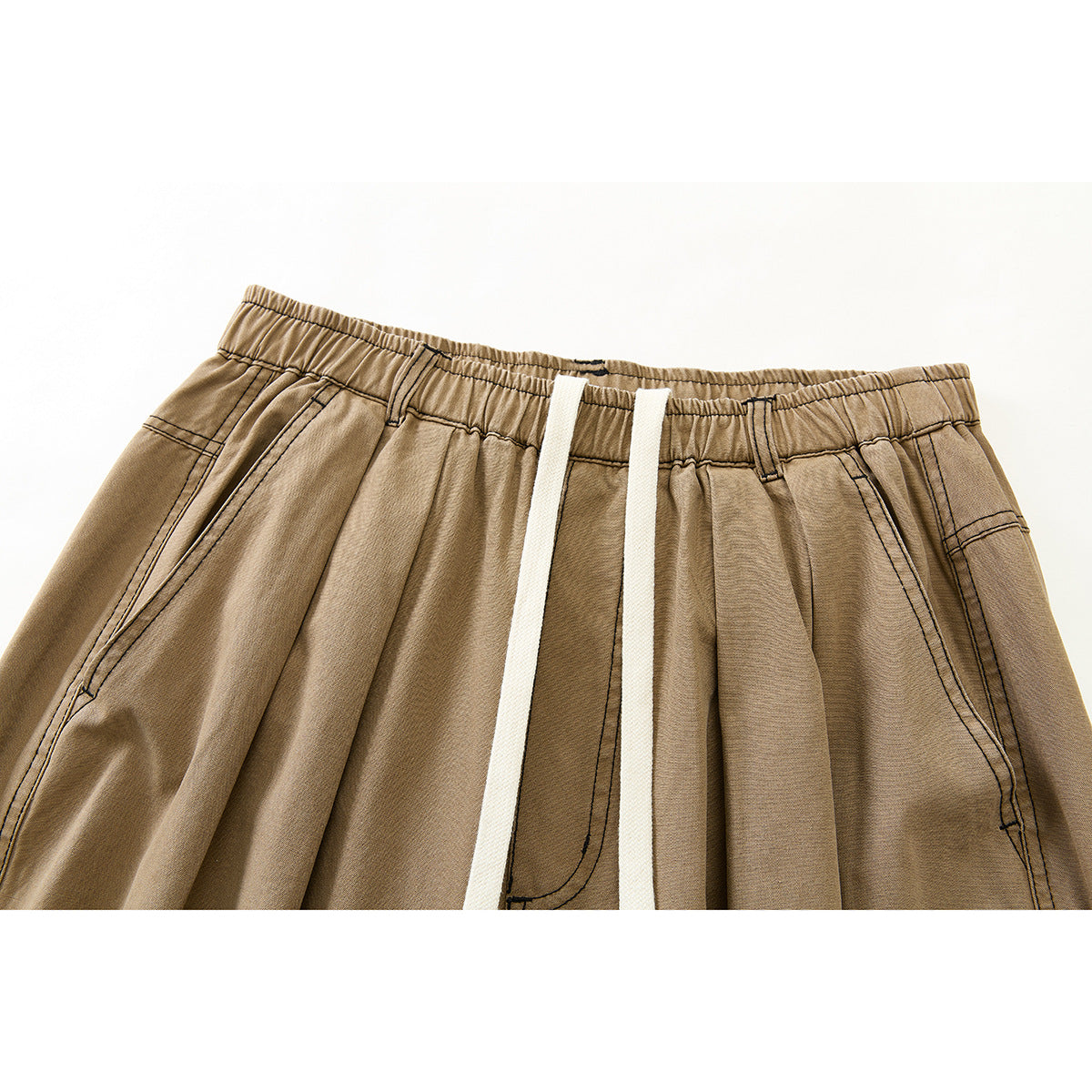 Close-up of tan wide-leg pants showing the elastic waistband, white drawstrings, pleats, and angled front pockets.