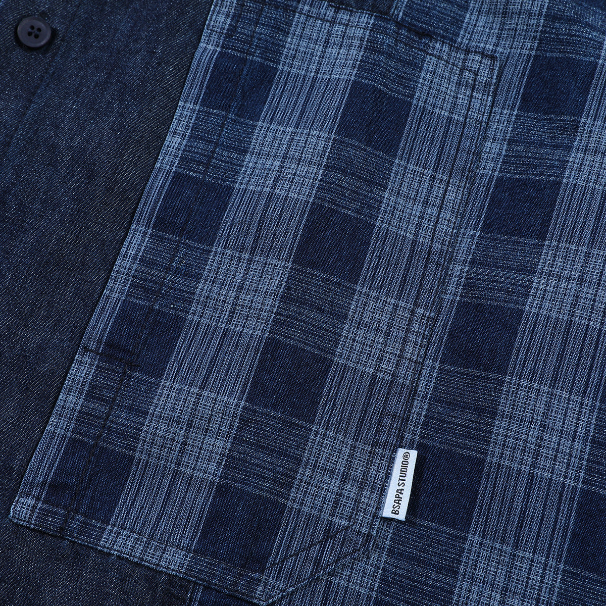 Close-up of a blue plaid shirt pocket with a small sewn label beside solid navy fabric.