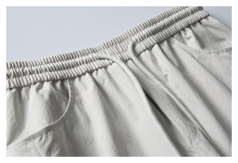 Close-up of light gray shorts showing the gathered elastic waistband, white drawstrings, and curved pocket opening.