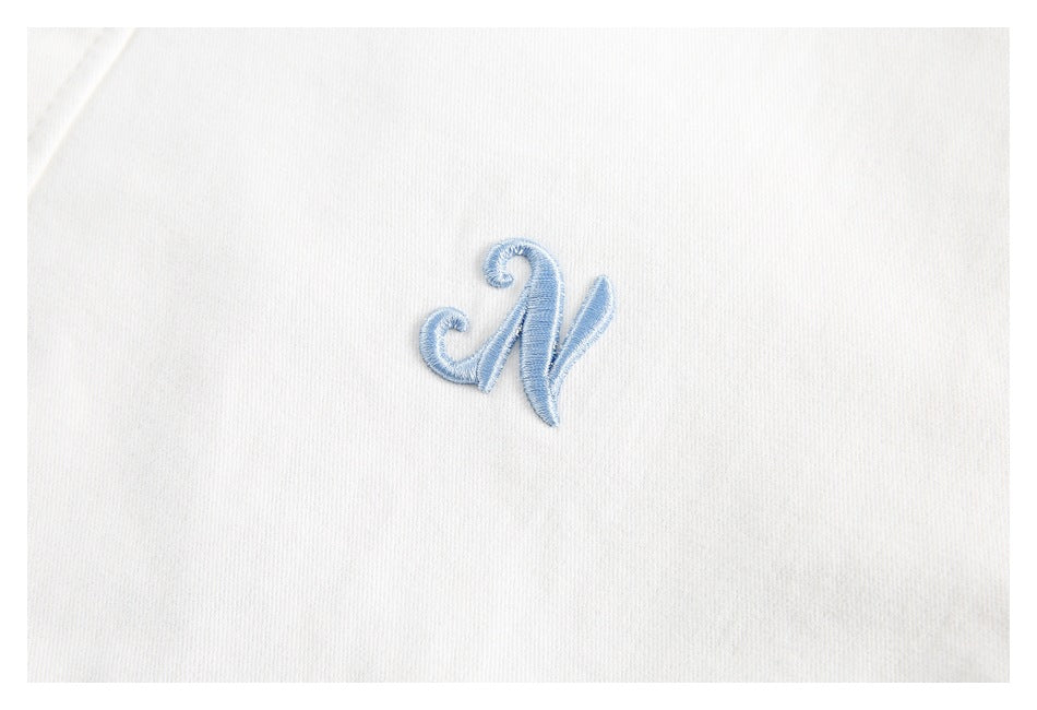 Close-up of a small light-blue embroidered monogram on white fabric.