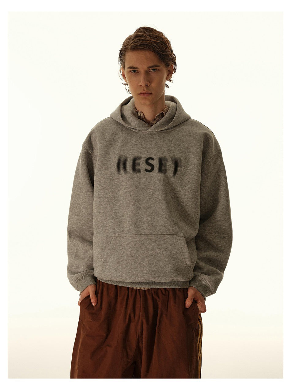 Closer view of a model wearing a light gray hoodie with a kangaroo pocket and blurred dark chest lettering.