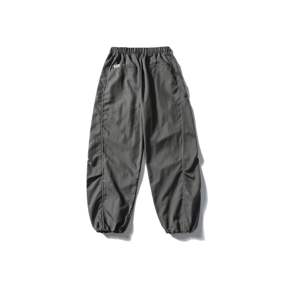 Charcoal gray relaxed pants shown from the back, with an elastic waist, two pockets, side piping and gathered cuffs.