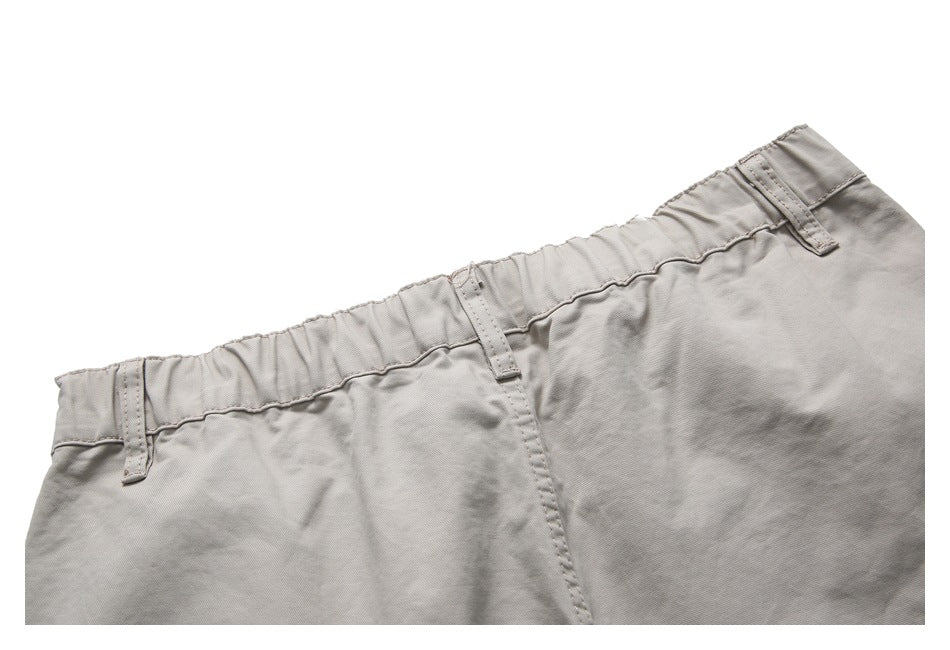 Close-up of light gray-beige shorts showing the gathered waistband, belt loops and stitching.