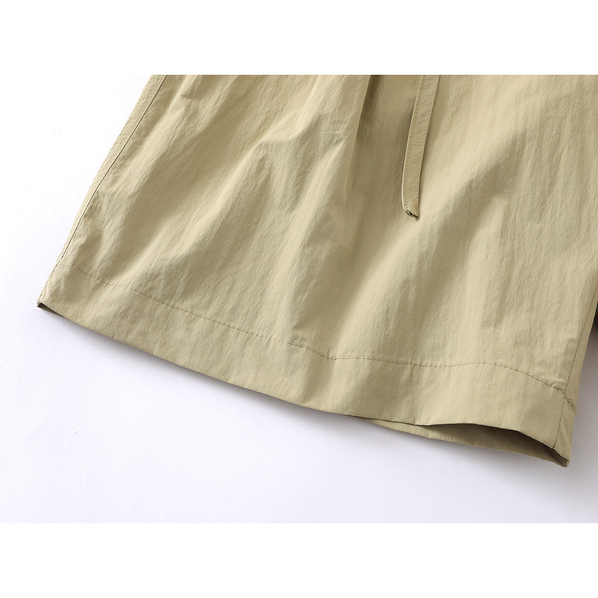 Close-up of the khaki shorts' wide leg and stitched hem, with a hanging belt end visible.