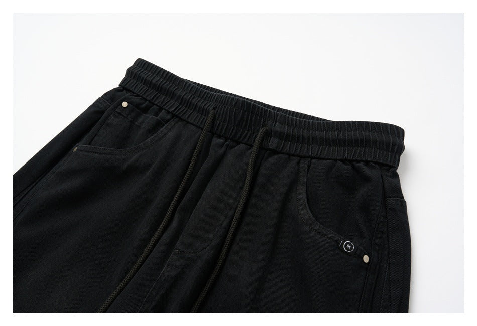 Angled front view of black pants with an elastic waist, drawstrings, and front pockets.