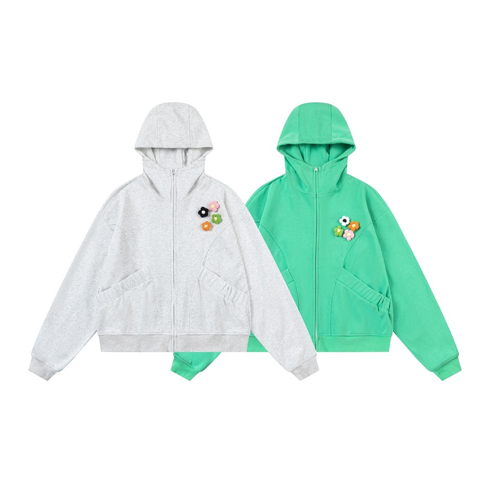 Two front-view hooded zip-up sweatshirts with flower appliqués, one light gray and one mint green.
