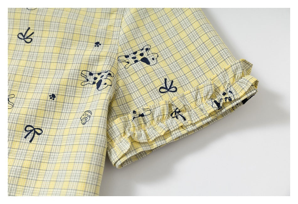 Close-up of a yellow plaid garment sleeve with navy dog and bow prints and a gathered ruffle cuff.