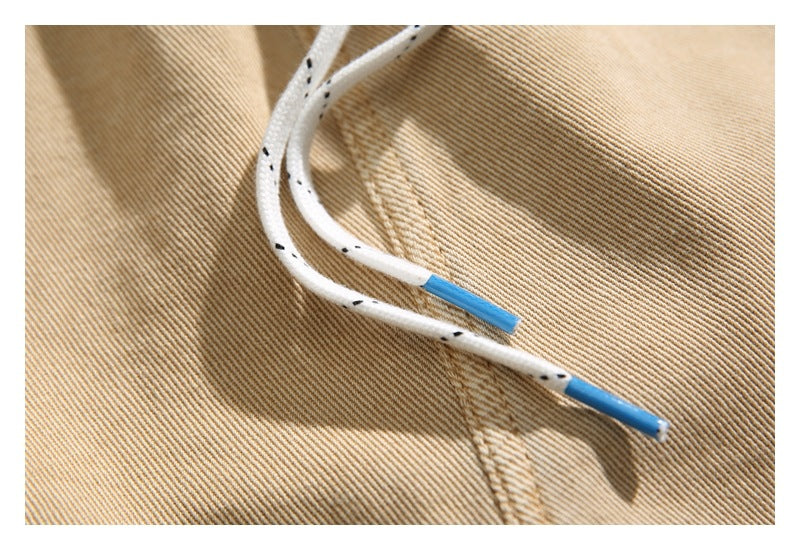 Close-up of white drawstrings with black flecks and blue tips against tan trouser fabric.