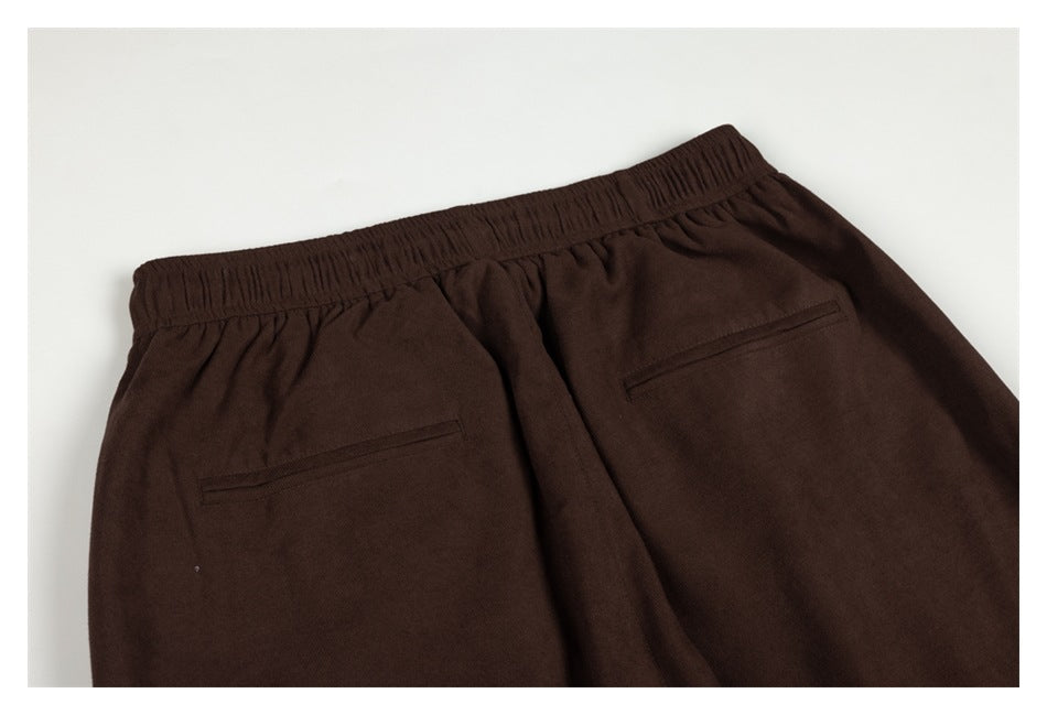 Back view of dark brown pants laid flat, showing an elastic waistband and two welt pockets.