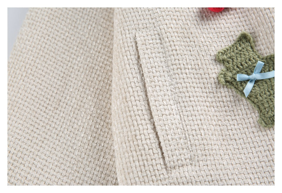 Close-up of ivory woven-texture fabric with a green knitted star appliqué and pale blue ribbon.