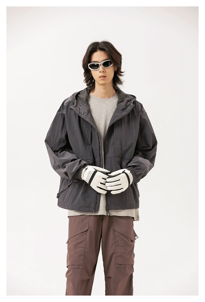 Model wearing an open charcoal hooded jacket with a front zip and pockets, paired with light gloves.