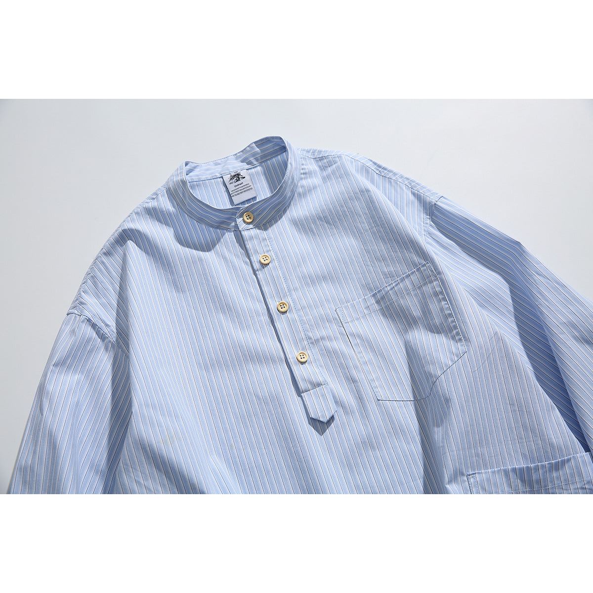 Close view of a light blue pinstriped shirt with a band collar, short button placket, and chest pocket.