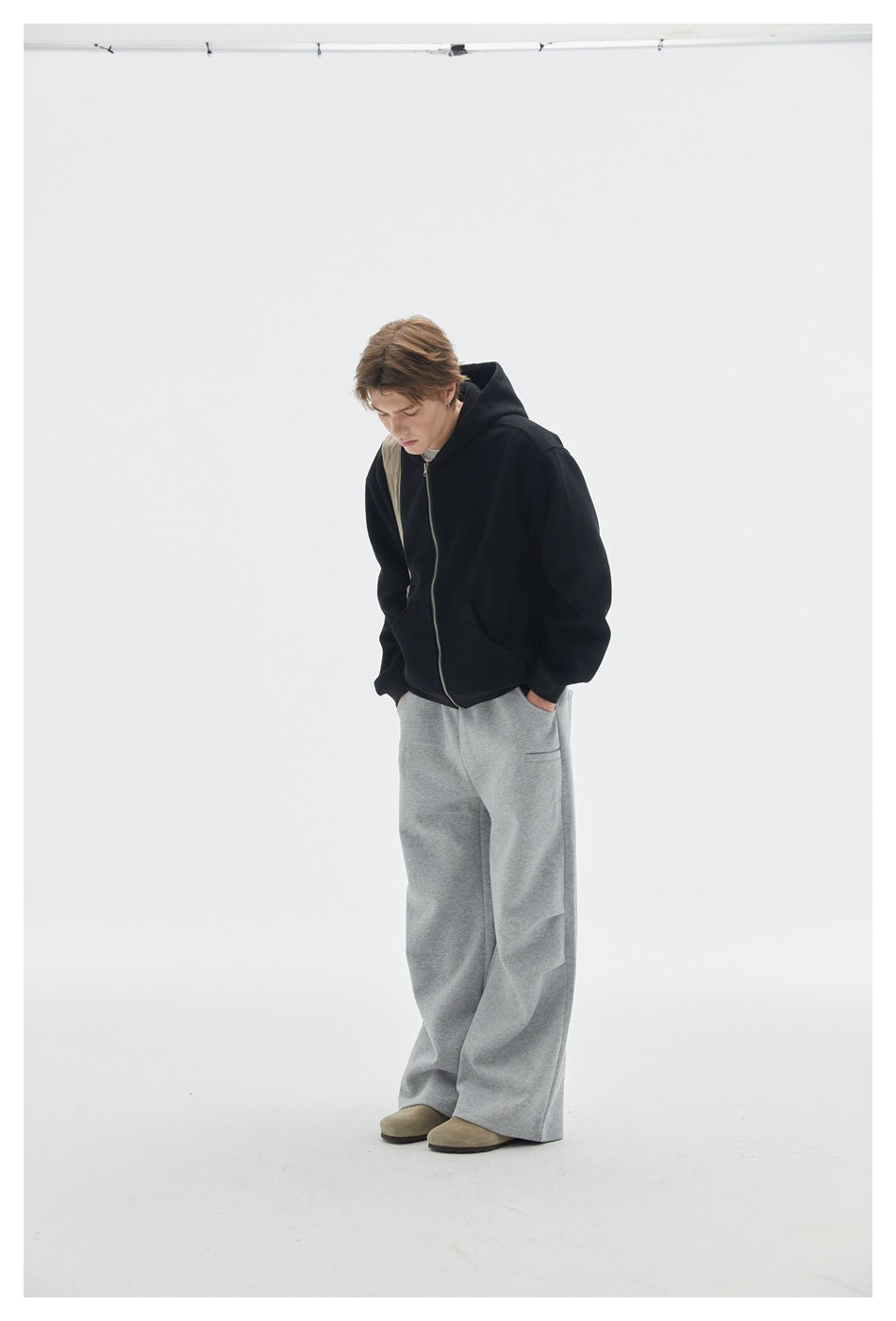 Model wearing a black zip-up hoodie with loose gray sweatpants, viewed at a slight angle.